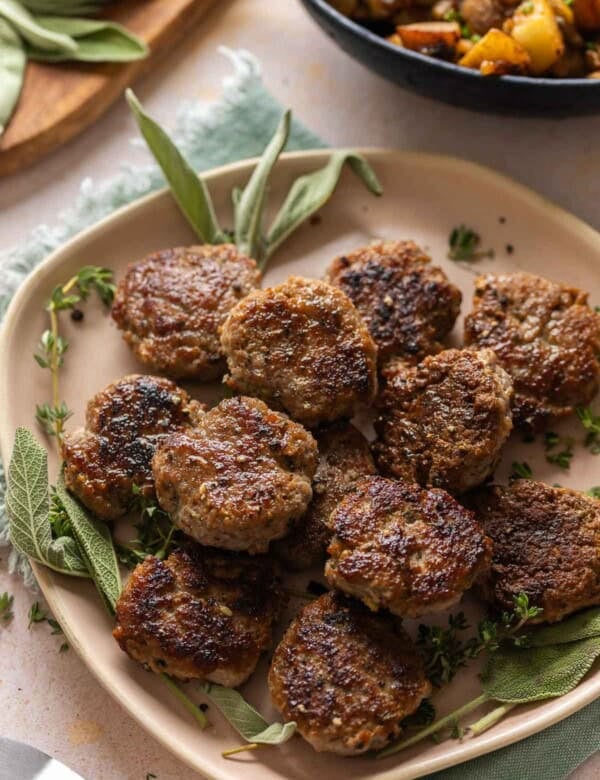 Turkey Maple Breakfast Sausage Patties on a serving plate with fresh sage and thyme.