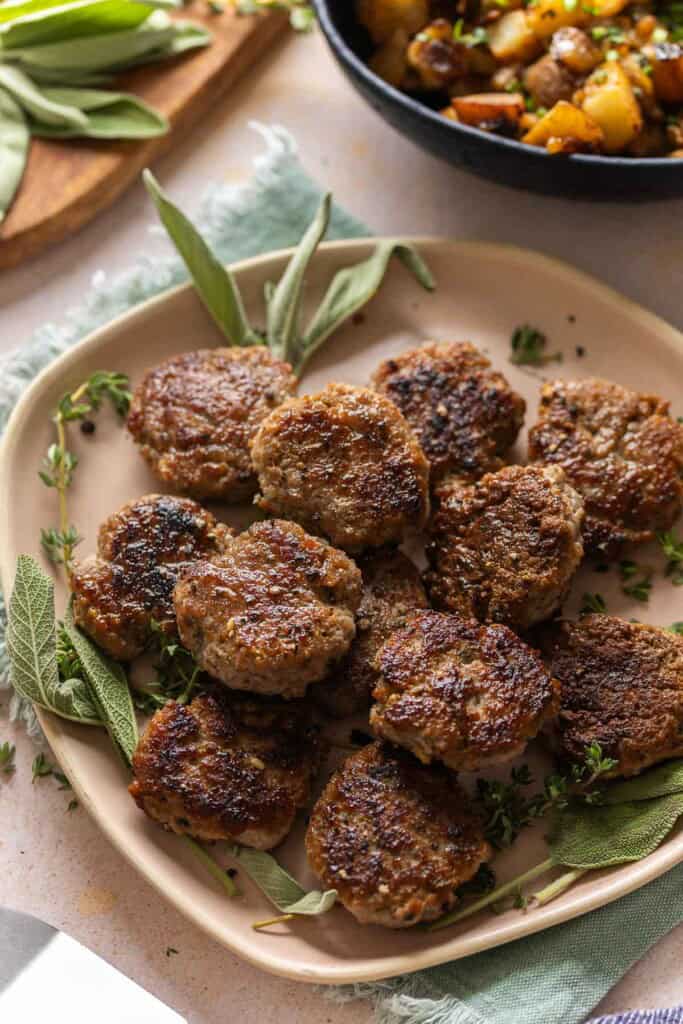 Turkey Maple Breakfast Sausage Patties on a serving plate with fresh sage and thyme.