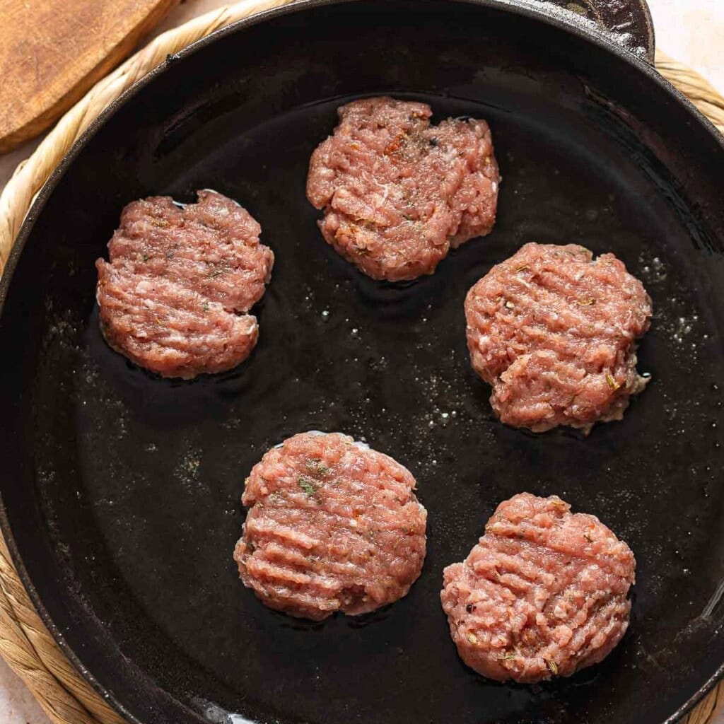 Four Turkey Maple Breakfast Sausage patties cooking in a cast iron skillet.
