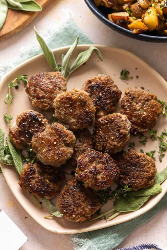 A plate full of Turkey Maple Breakfast Sausage Patties with fresh sage and thyme.