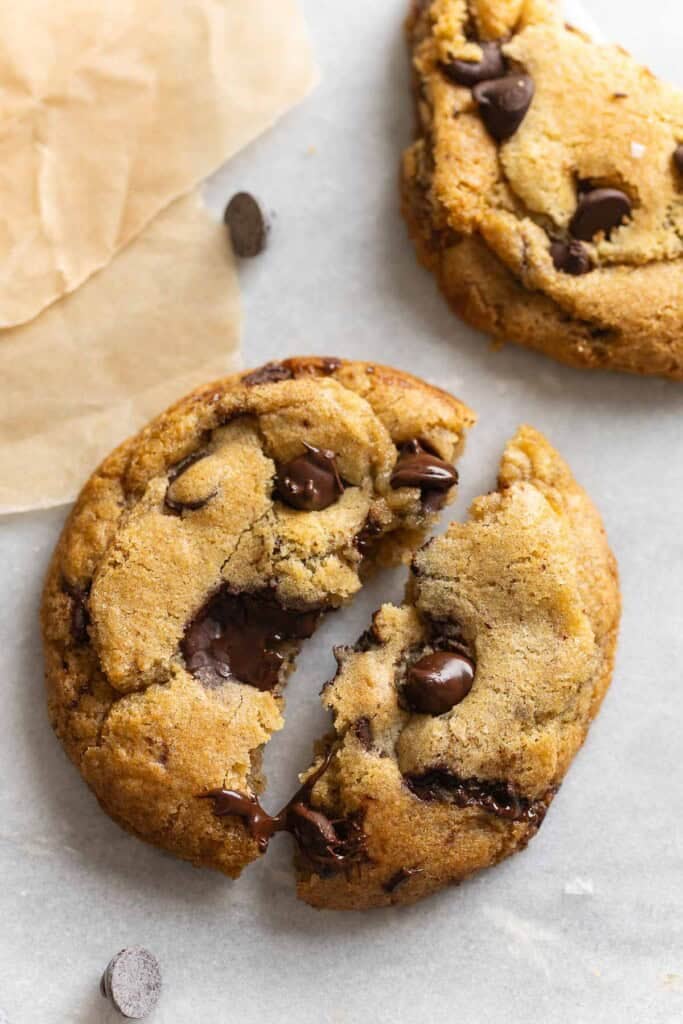 A gluten free brown butter chocolate chip cookie torn into 2 halves with melted chocolate