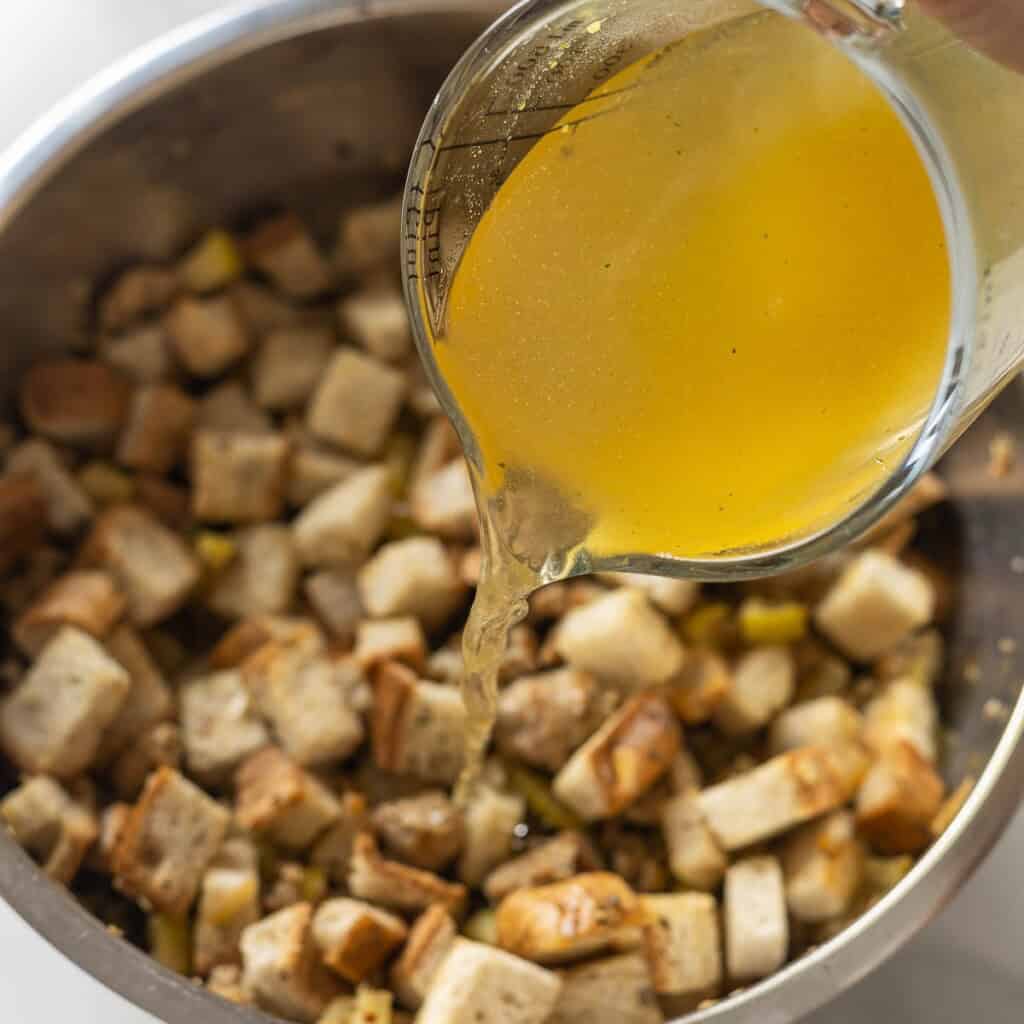 Chicken stock pouring into a bowl full of gluten free stuffing.