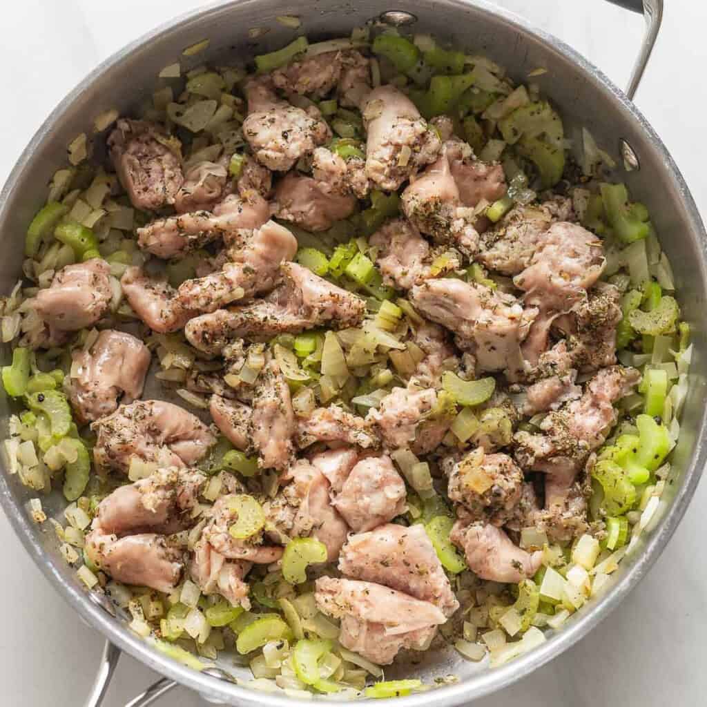A stainless steel pan full of sautéed onion, celery, sausage meat and herbs.