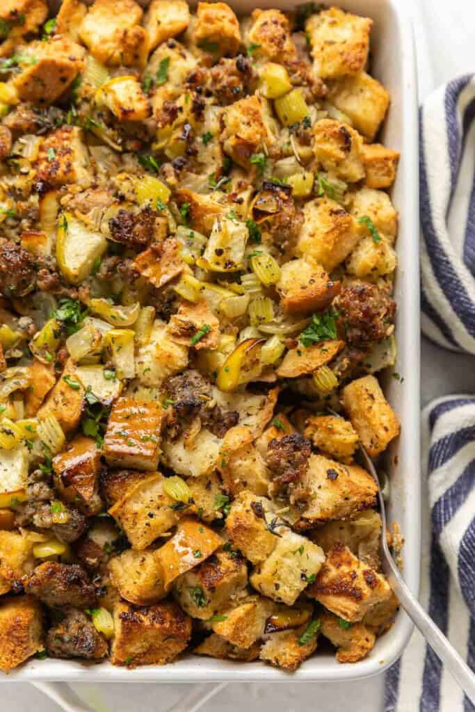 Gluten Free Stuffing with Sausage & Apple in a casserole dish with a serving spoon in the corner of the dish.