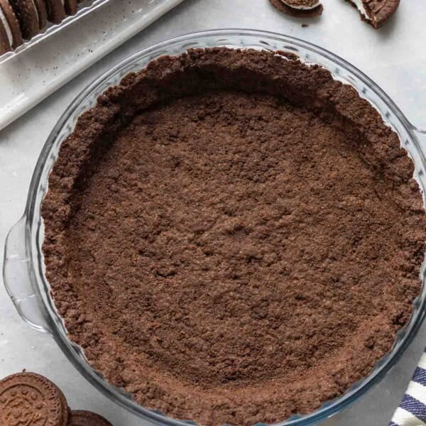 A Gluten Free Oreo Cookie Crust in a pie dish surrounded by gluten free oreos