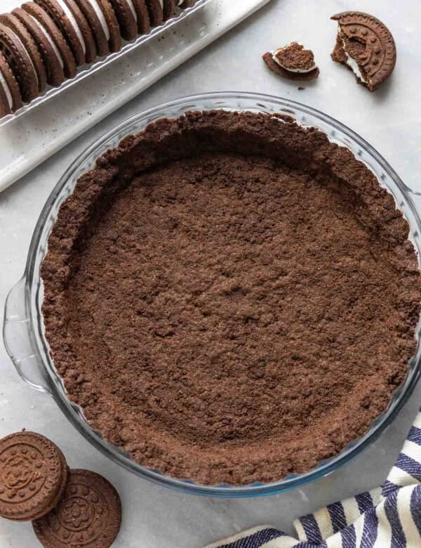 A Gluten Free Oreo Cookie Crust in a pie dish surrounded by gluten free oreos