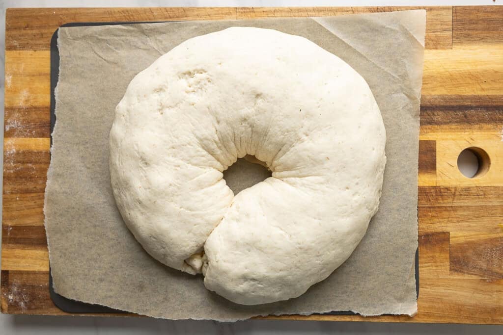 Gluten free pizza dough filled with sausage and cheese shaped into a donut on a baking sheet after it's had time to rise.