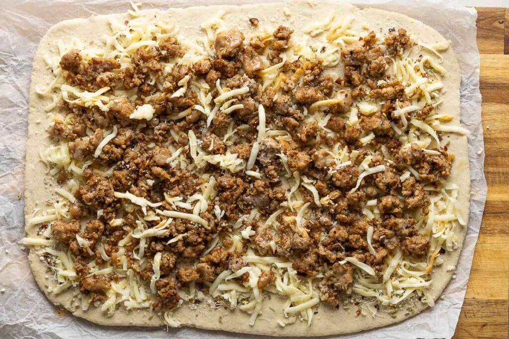 Gluten free dough rolled out into a 12-inch x 16-inch shape with cooked sausage and shredded cheese over the top.