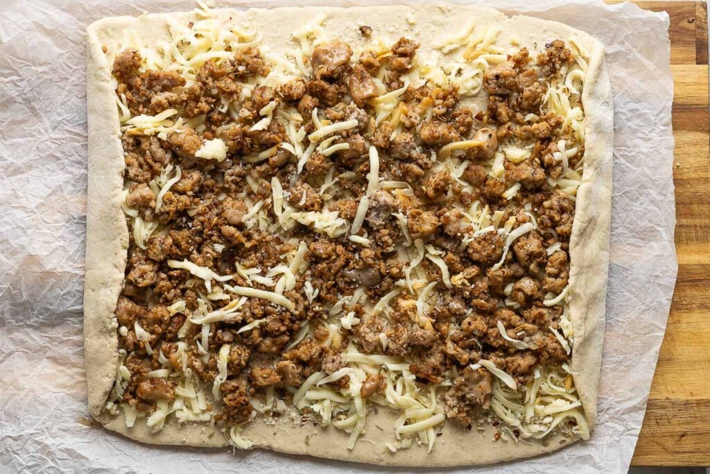 Gluten free dough rolled out in a large rectangle & filled with cheese and sausage and rolled up in a log shape. The sides folded in.