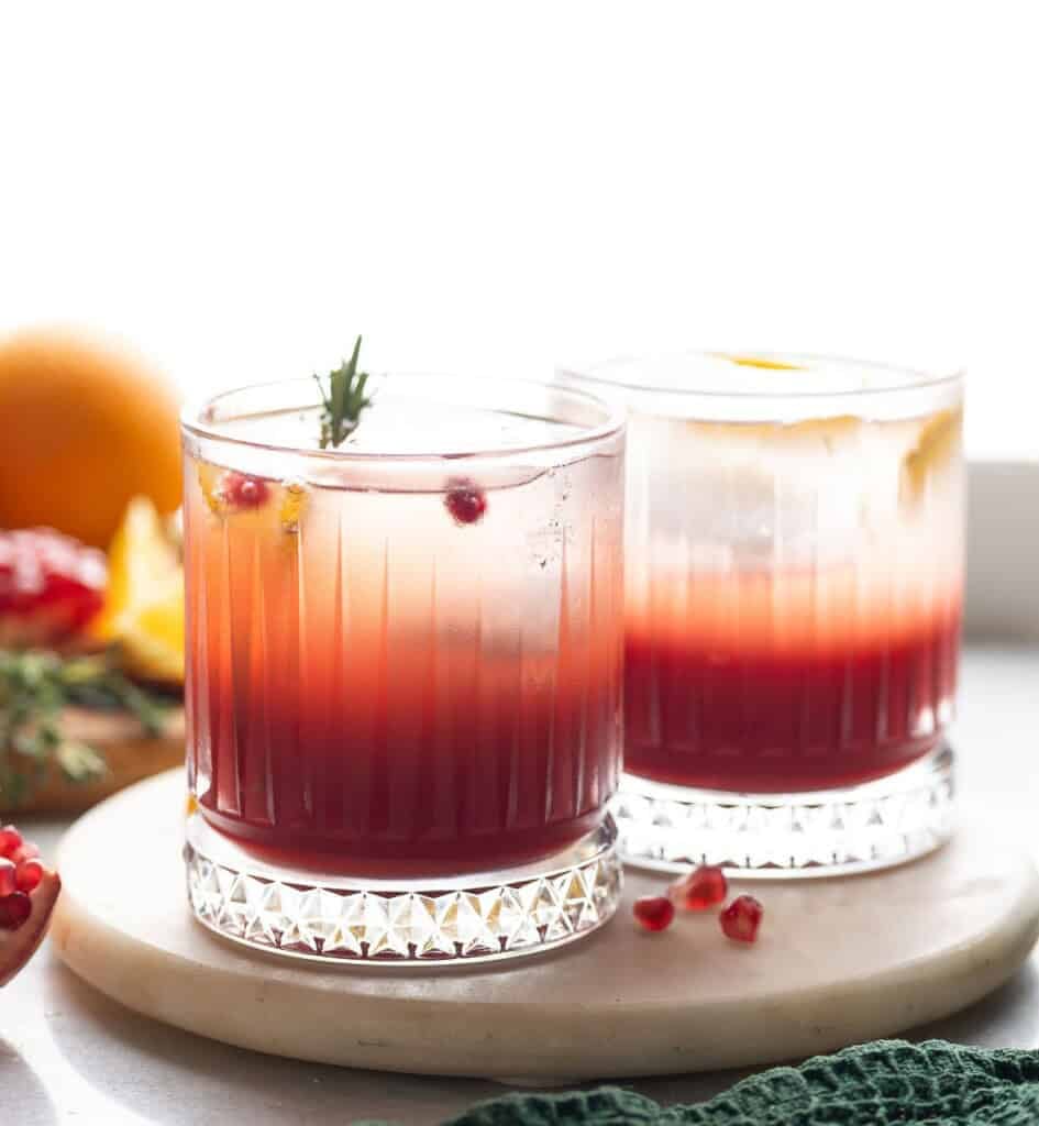 Two glasses of Honeyed Herbal Orange & Pomegranate Mocktails on a serving tray