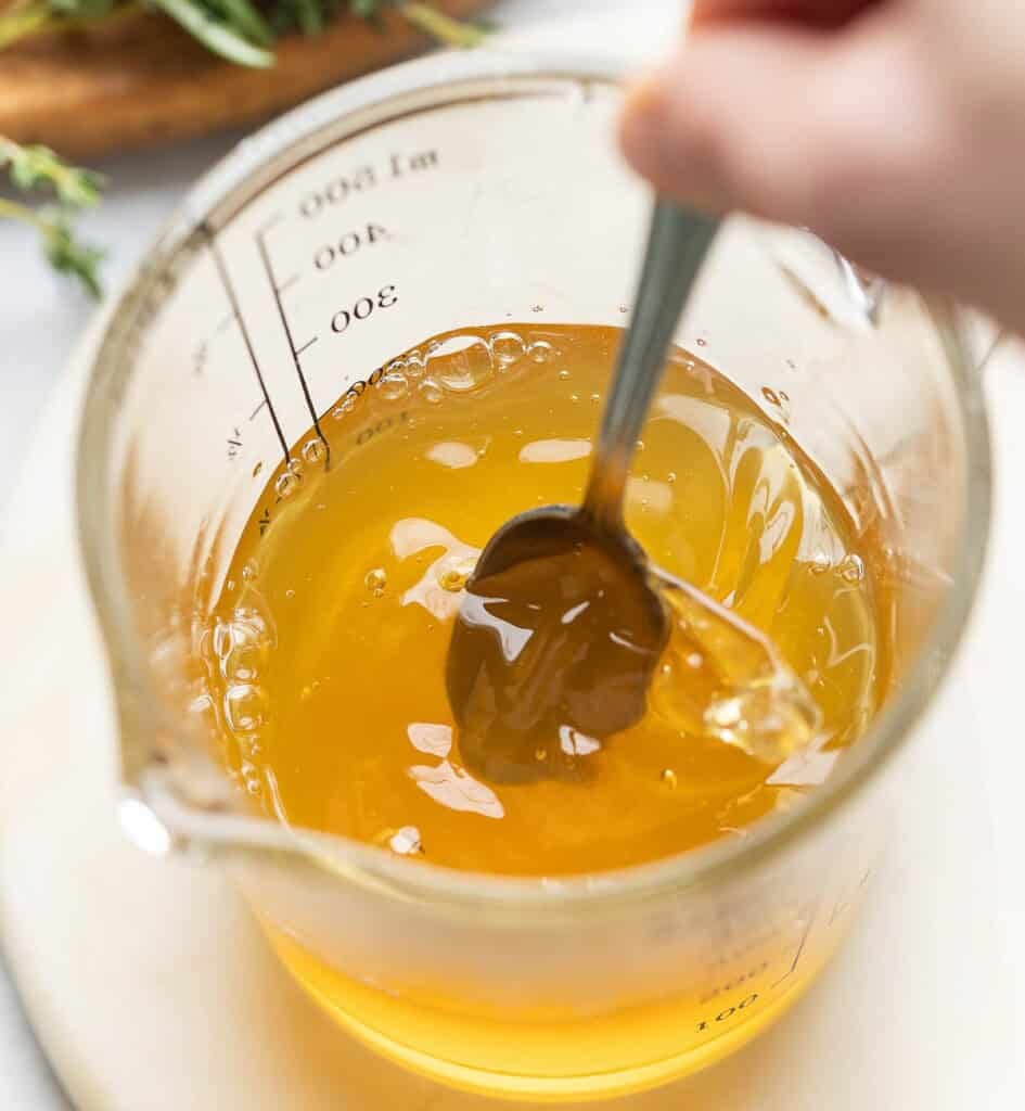 A spoon stirring honey into water to make simple syrup
