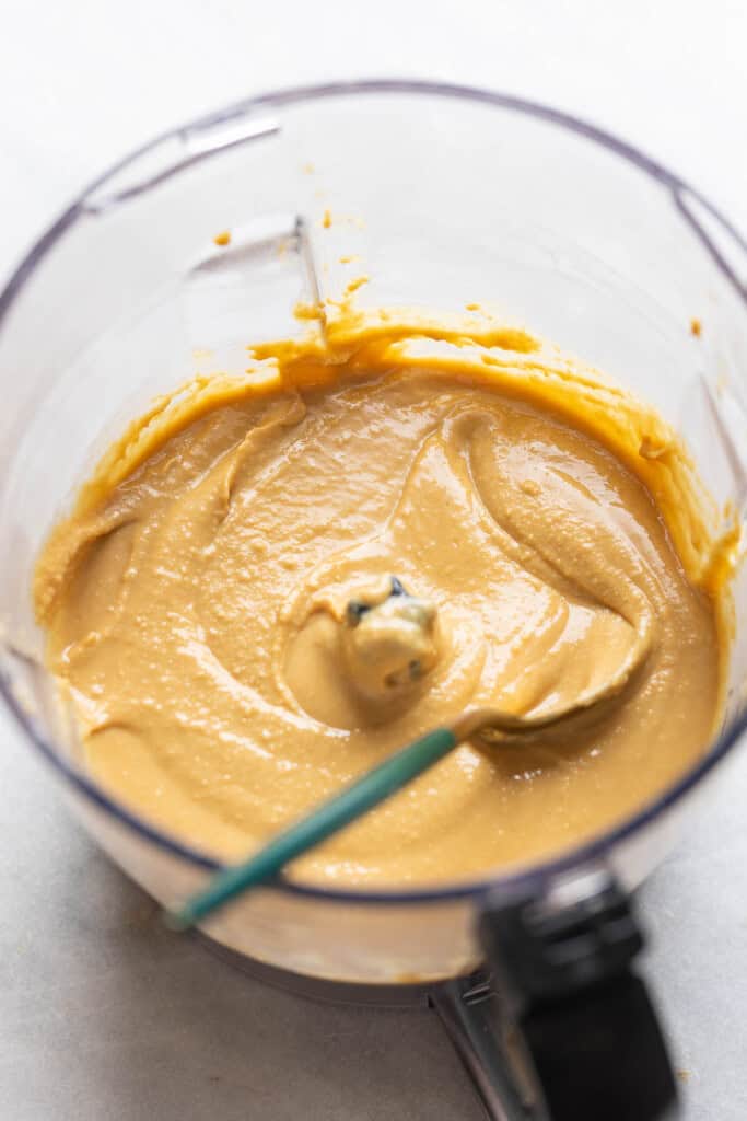 Homemade peanut butter in a food processor bowl with a spoon inside the bowl