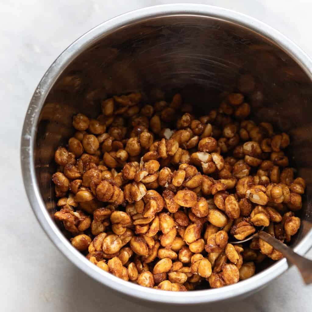 Honey roasted peanuts added to a large mixing bowl with a spoon - mixing together to break up the sticky chunks
