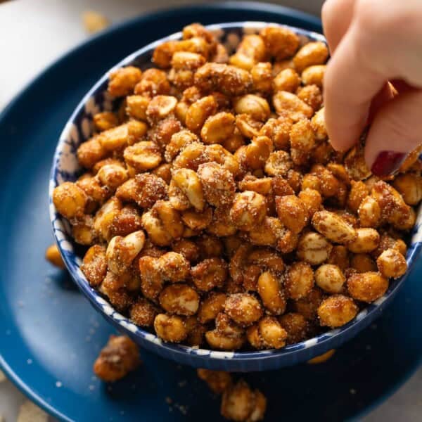 A hand picking up some honey roasted peanuts from a serving bowl
