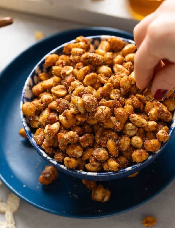 A hand picking up some honey roasted peanuts from a serving bowl