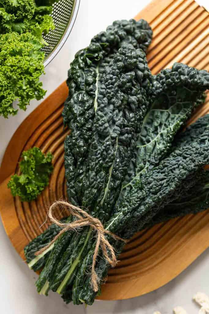 cavolo nero kale in a bundle on a serving board with curly leaf kale in the back