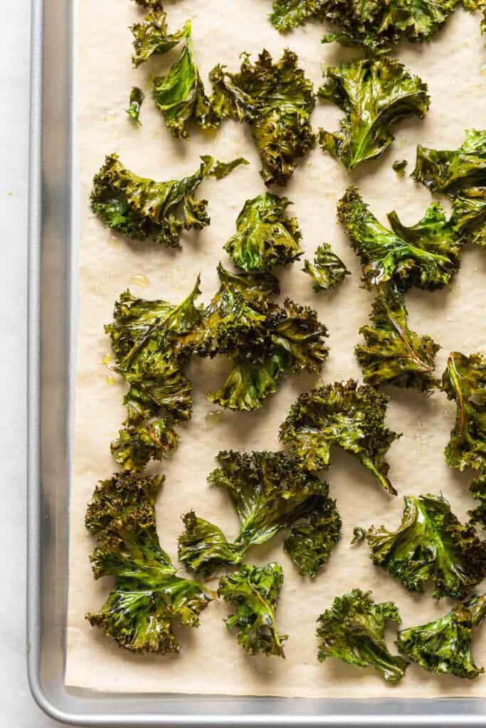 Baked kale chips seasoned with salt and pepper spread out on a baking sheet