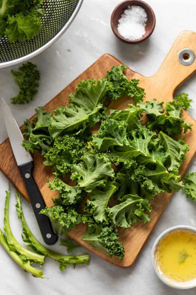 Raw kale on a cutting board with the hard ribs removed and torn into small pieces