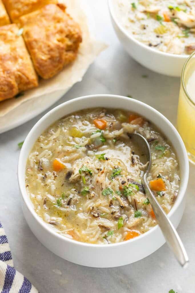 Instant pot chicken & wild rice soup in a bowl topped with fresh chopped parsley and bread on the side and bread in the back.