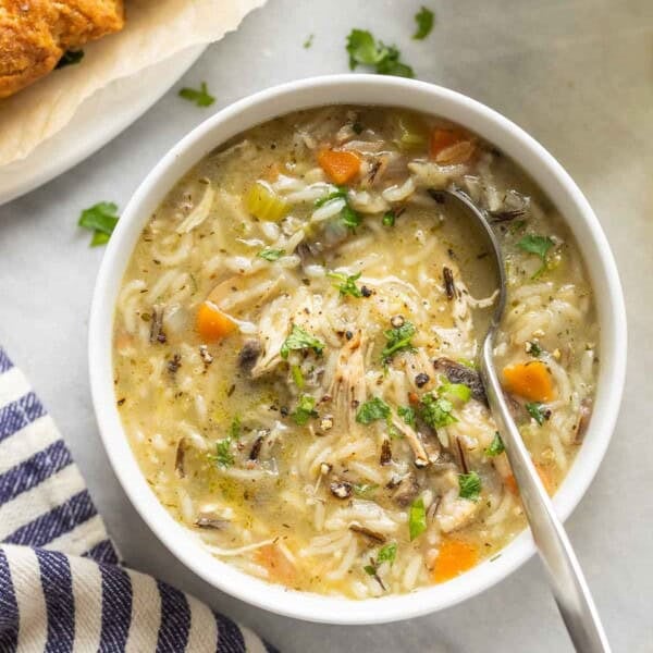 Instant pot chicken & wild rice soup in a bowl topped with fresh chopped parsley and bread on the side.
