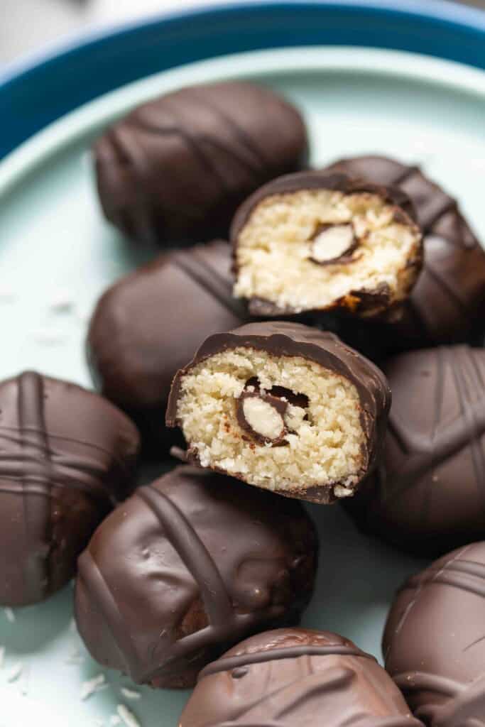 A homemade Almond Joy Snack Bites cut in half to show off the coconut almond filling with a chocolate covered almond hidden in the middle.