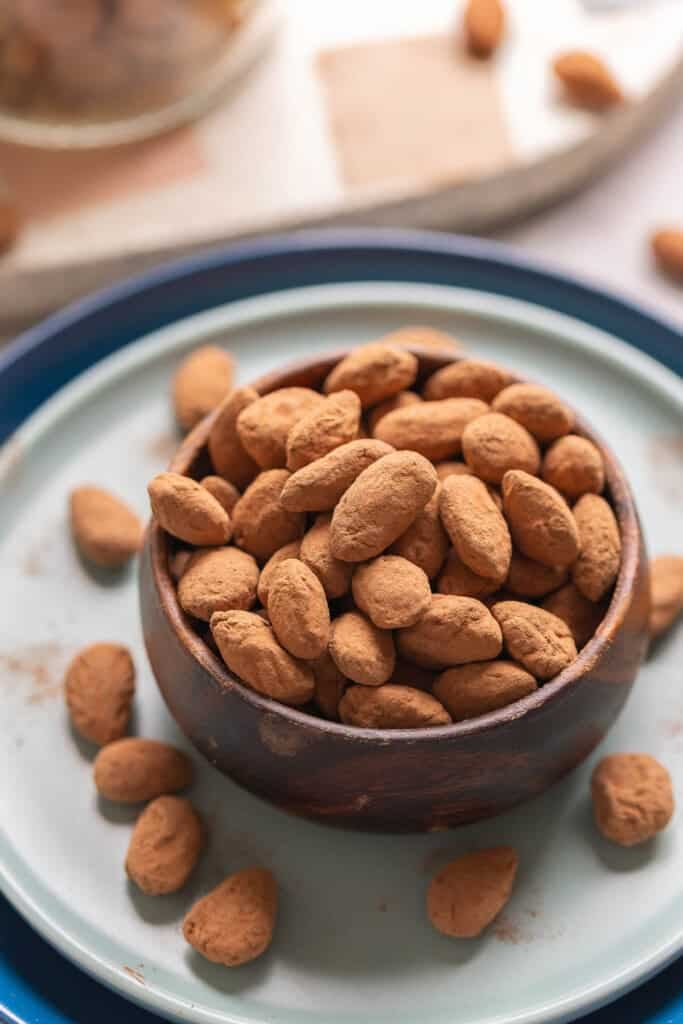Chocolate covered almonds dusted with cocoa powder in a small bowl on a plate