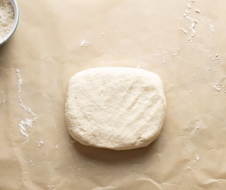 Gluten free pizza dough on a floured piece of baking paper.