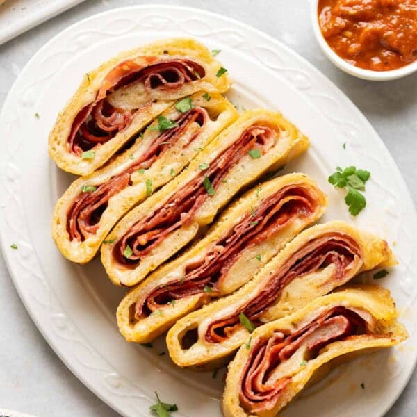 Gluten free Stromboli slices filled with melted cheese and deli meats and a small bowl of marinara on the side.