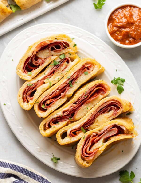 Gluten free Stromboli slices filled with melted cheese and deli meats and a small bowl of marinara on the side.