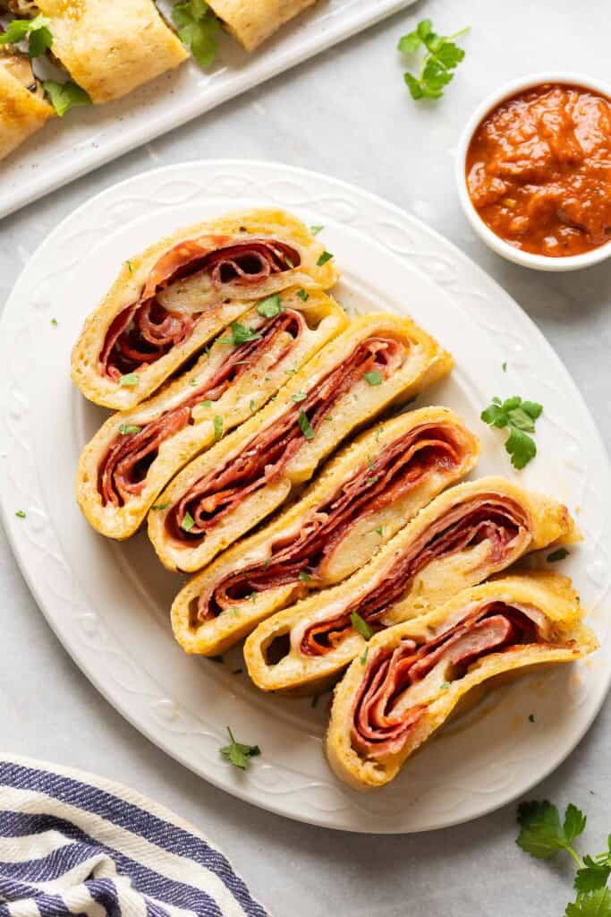 Gluten free Stromboli slices filled with melted cheese and deli meats and a small bowl of marinara on the side.