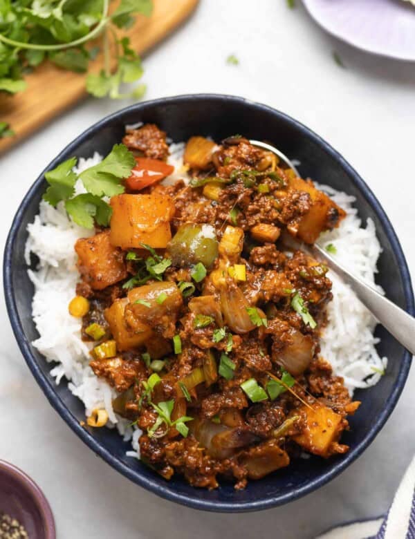 Ground Beef & Potatoes in a serving bowl over a bed or rice with fresh cilantro and spring onions