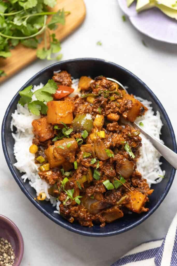 Ground Beef & Potatoes in a serving bowl over a bed or rice with fresh cilantro and spring onions