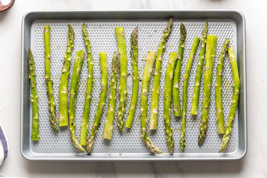 Raw asparagus seasoned with salt, pepper and olive oil on a baking sheet