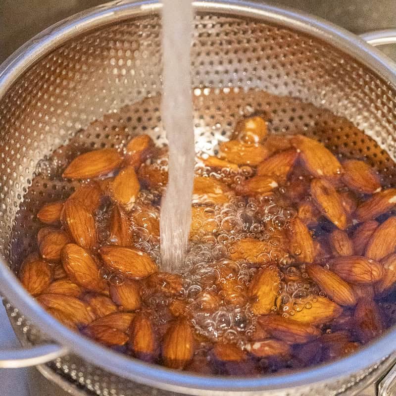 Water running over a colander full of boiled almonds