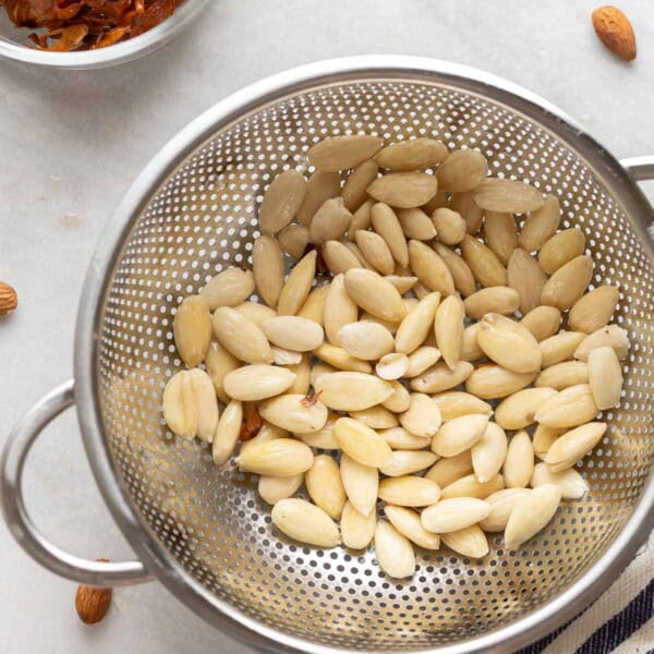 A colander full of blanched almonds with the almond skins in a separate bowl on the side.