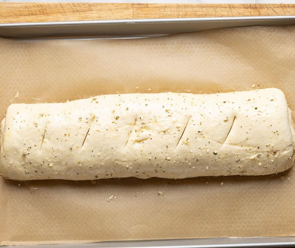 Unbaked gluten free stromboli with slits cut into the top of the dough and brushed with an egg wash made with egg, parmesan cheese and dried herbs.