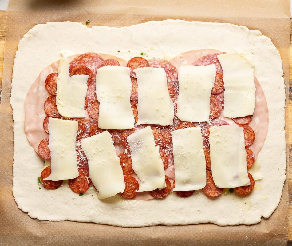 Gluten free pizza dough rolled out into a large rectangle and topped with alternating layers of deli meat and cheese in the middle before rolling into a stromboli.