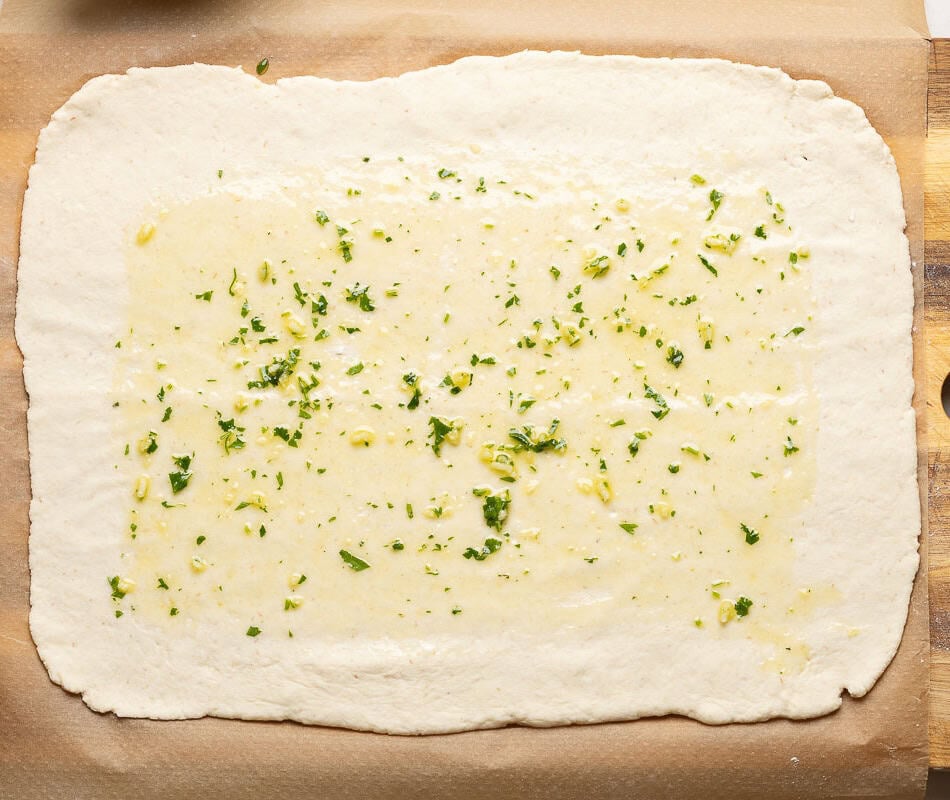 Gluten free pizza dough rolled out into a large rectangle and brushed with olive oil, garlic and fresh parsley.