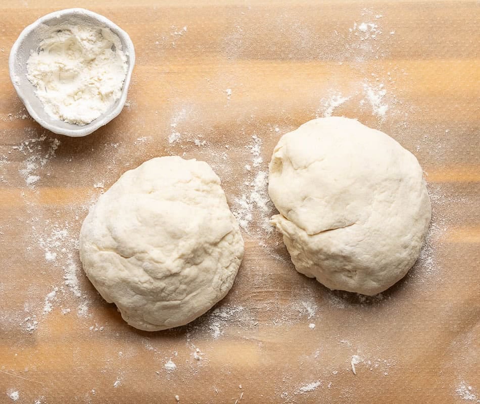 Gluten free Stromboli dough divided into 2 equal sized pieces on a lightly floured surface.