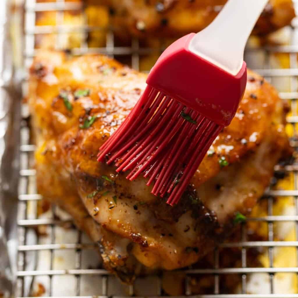 Lemon sauce brushing over a baked lemon pepper chicken thigh.