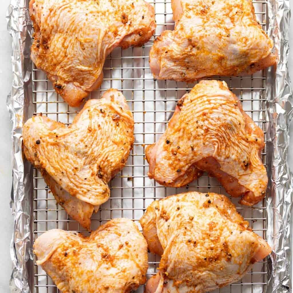 Marinated chicken thighs on a wire rack over a baking sheet covered in foil.