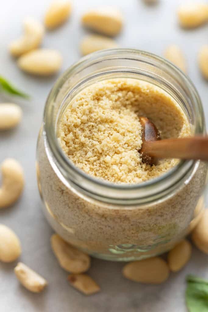 A jar of Homemade vegan parmesan cheese surrounded by cashews and almonds