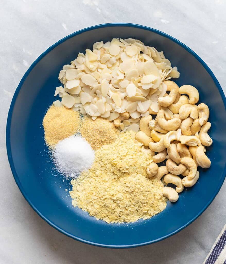 A bowl full of ingredients needed to make vegan parmesan cheese: raw cashews, almonds, nutritional yeast, salt, onion powder & garlic powder.