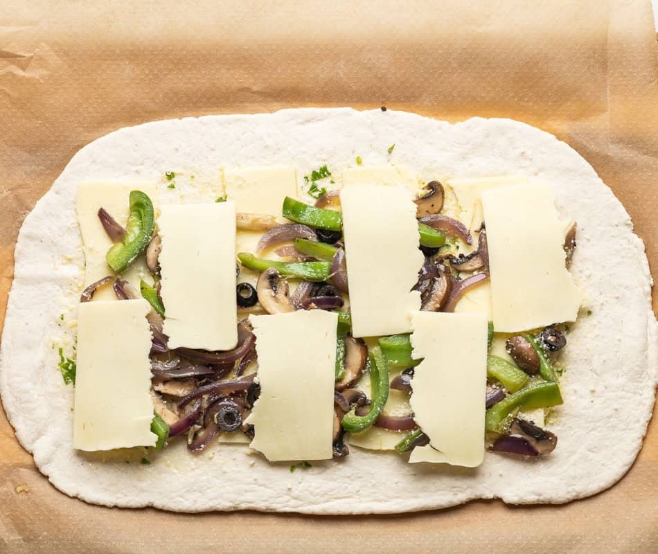 Gluten free pizza dough rolled out into a large rectangle and topped with alternating layers of cheese and sautéd veggies in the middle before rolling into a stromboli.