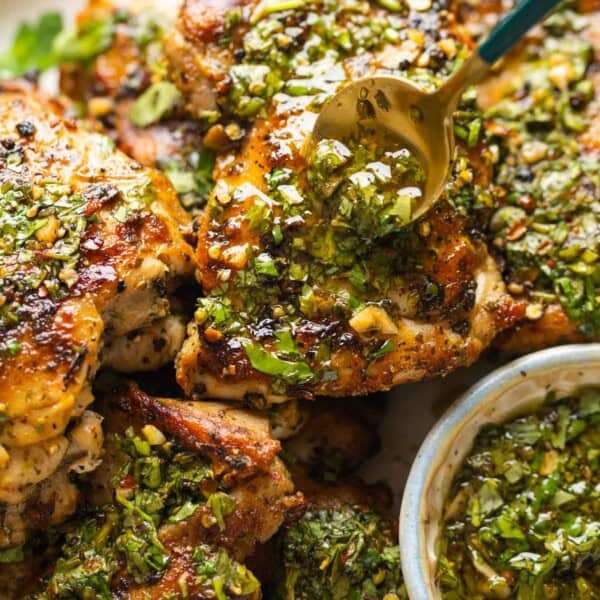A spoon adding more chimichurri sauce over cooked chicken thighs