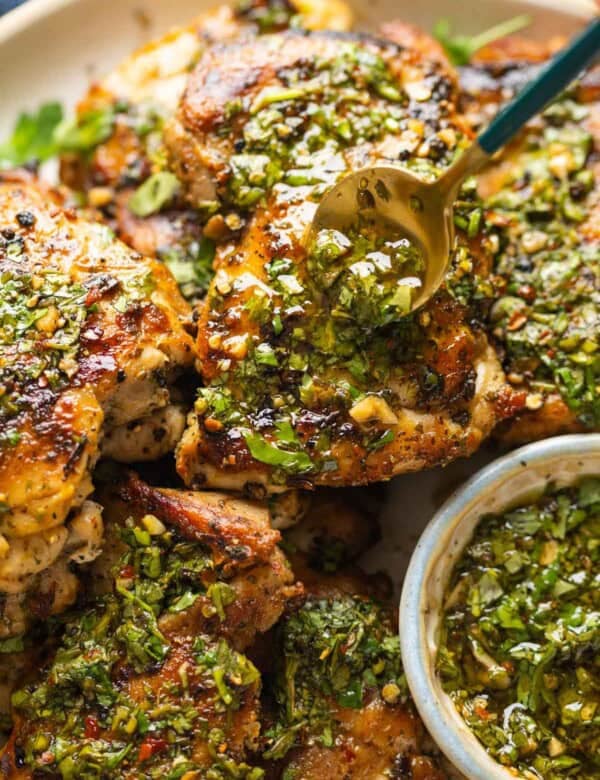A spoon adding more chimichurri sauce over cooked chicken thighs