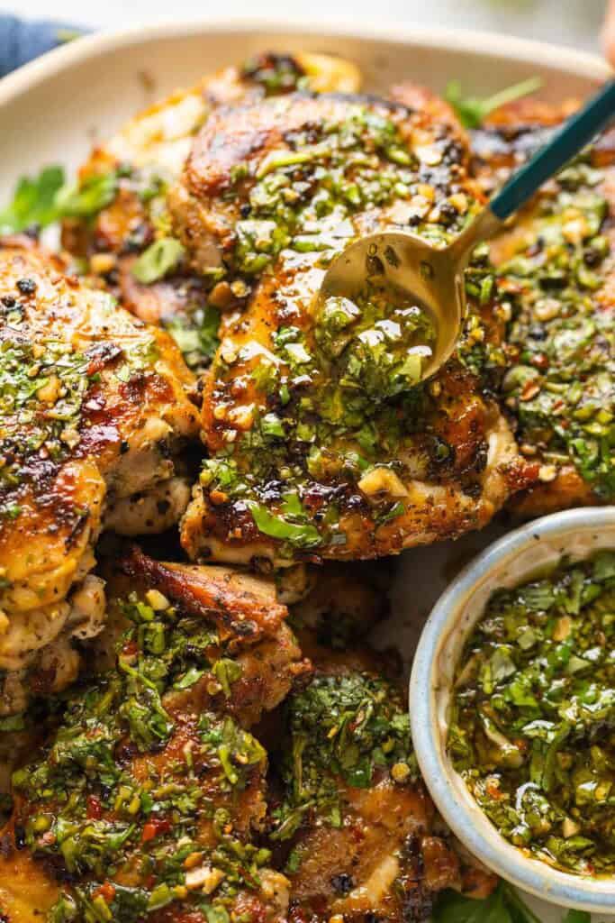 A spoon adding more chimichurri sauce over cooked chicken thighs