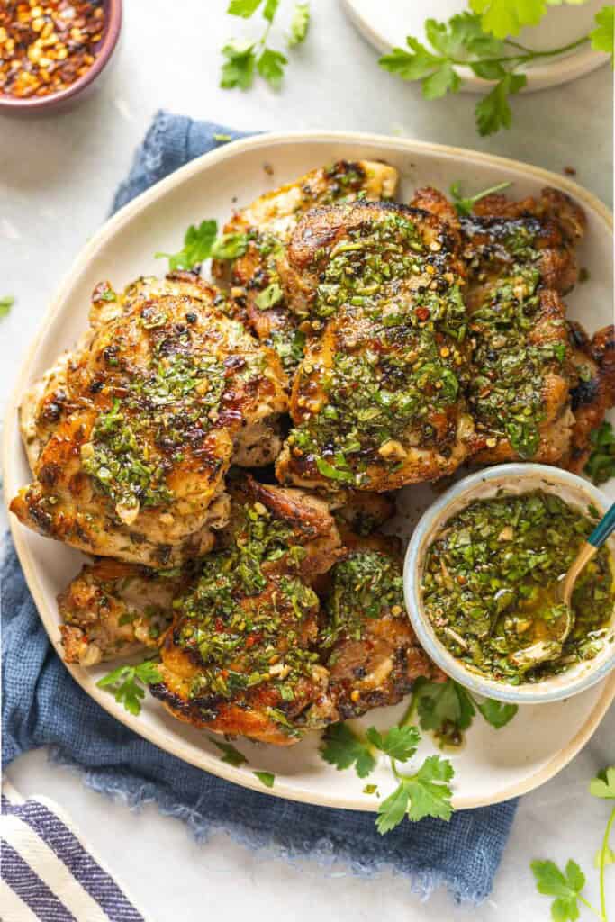 A plate full of grilled chimichurri chicken thighs topped with fresh chimichurri