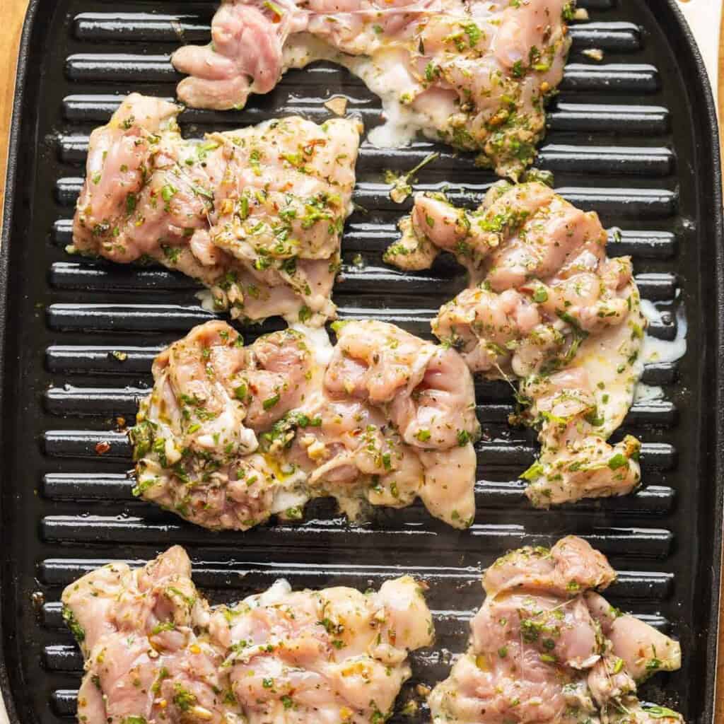 Boneless, skinless chicken thighs cooking on a griddle pan