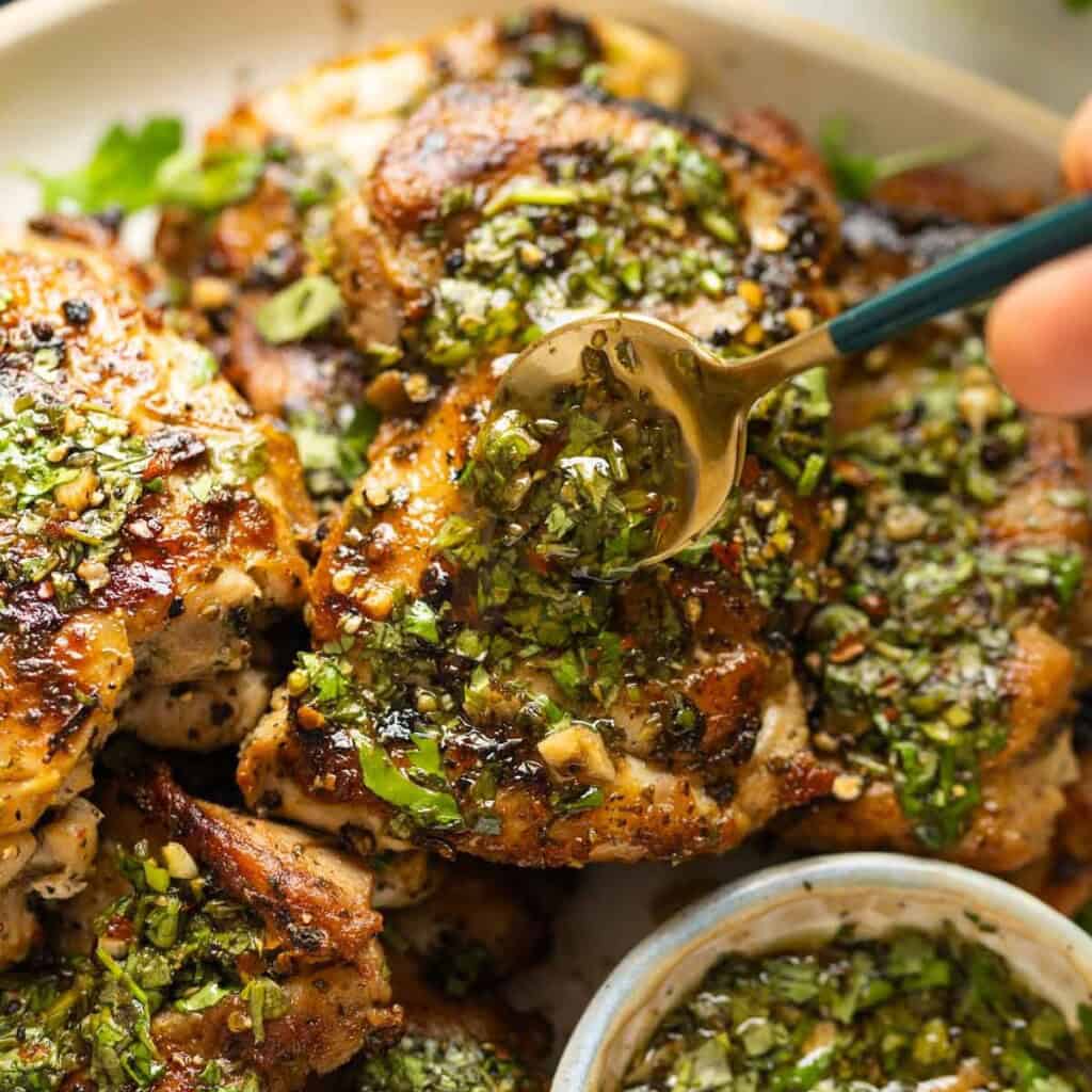 Chimichurri sauce spooned over cooked chicken thighs